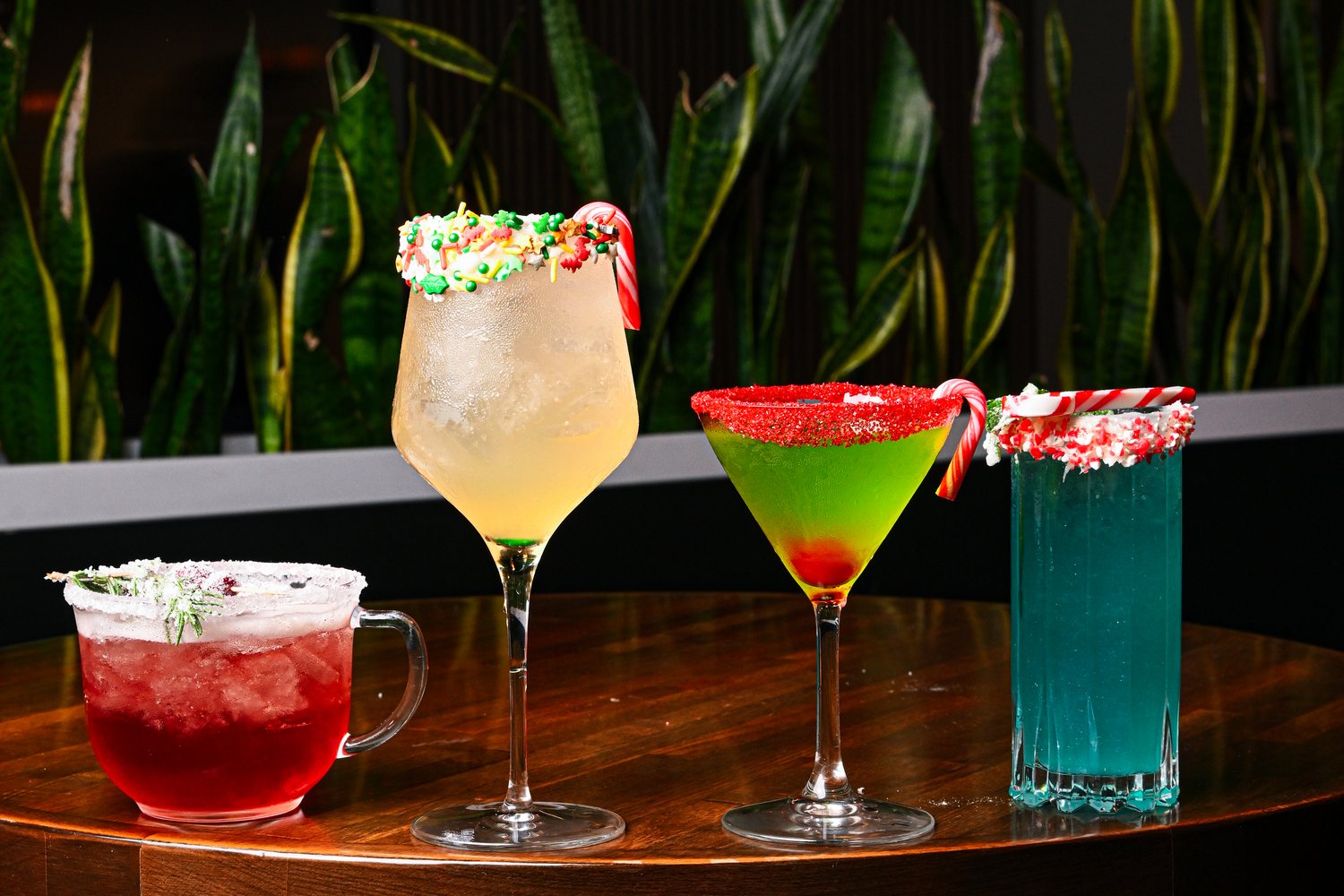 Four colorful finished cocktails on a dark restaurant bar