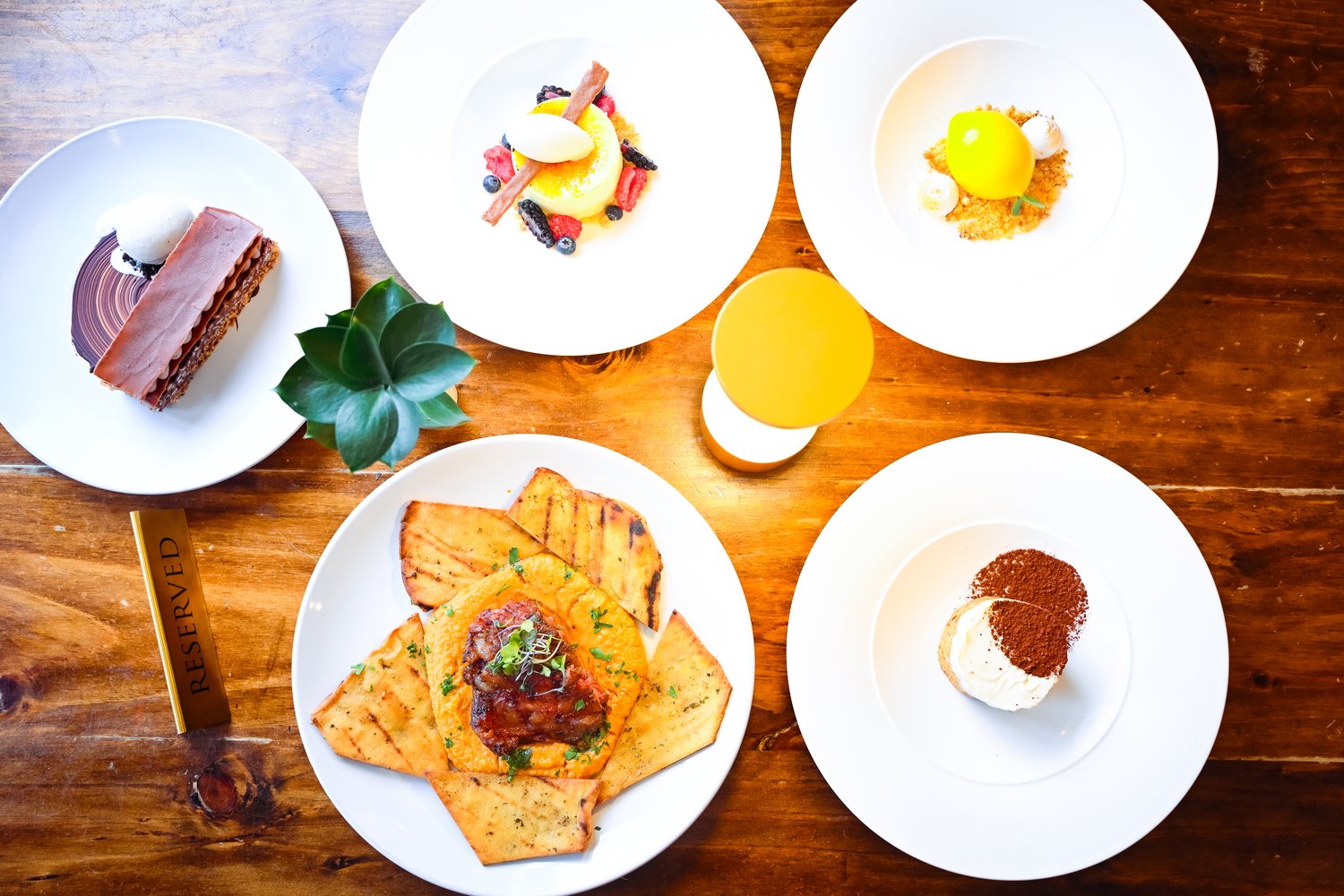 Overhead table with several plated dishes, desserts, and a drink