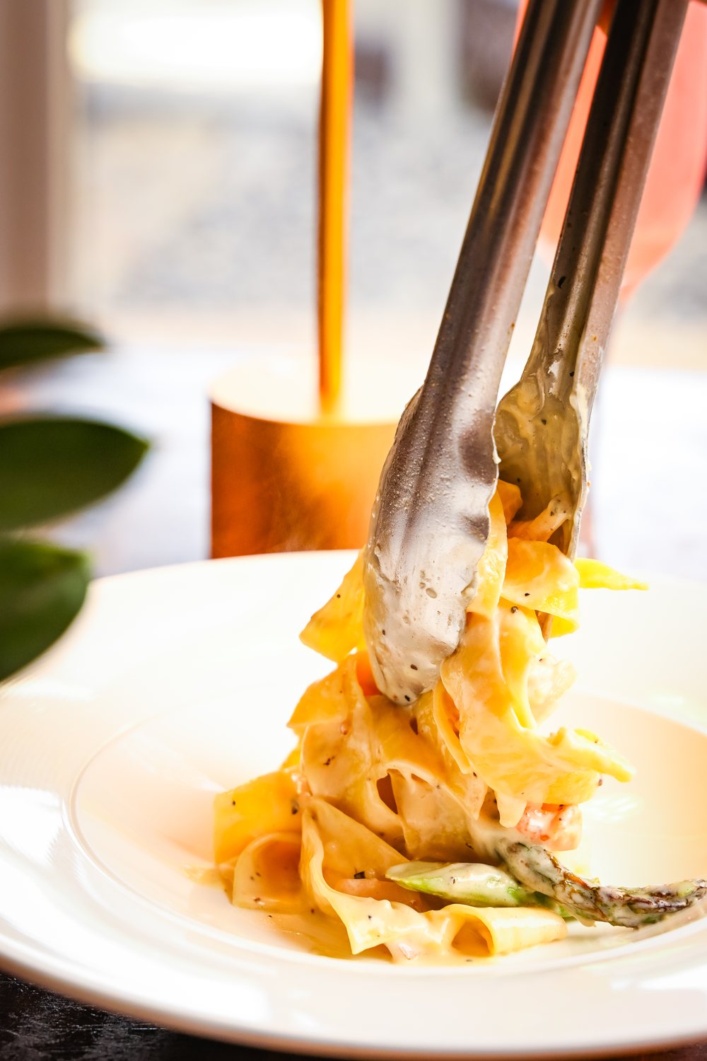 Pasta lifted from a plate with serving tongs