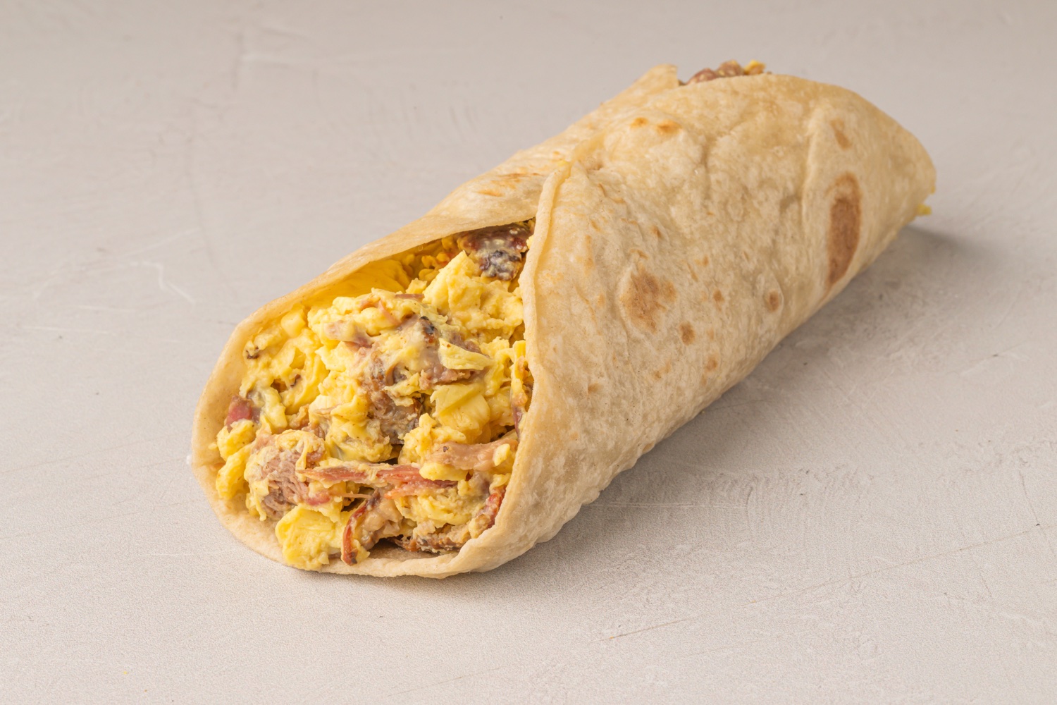 Breakfast burrito with eggs and meat on a light surface