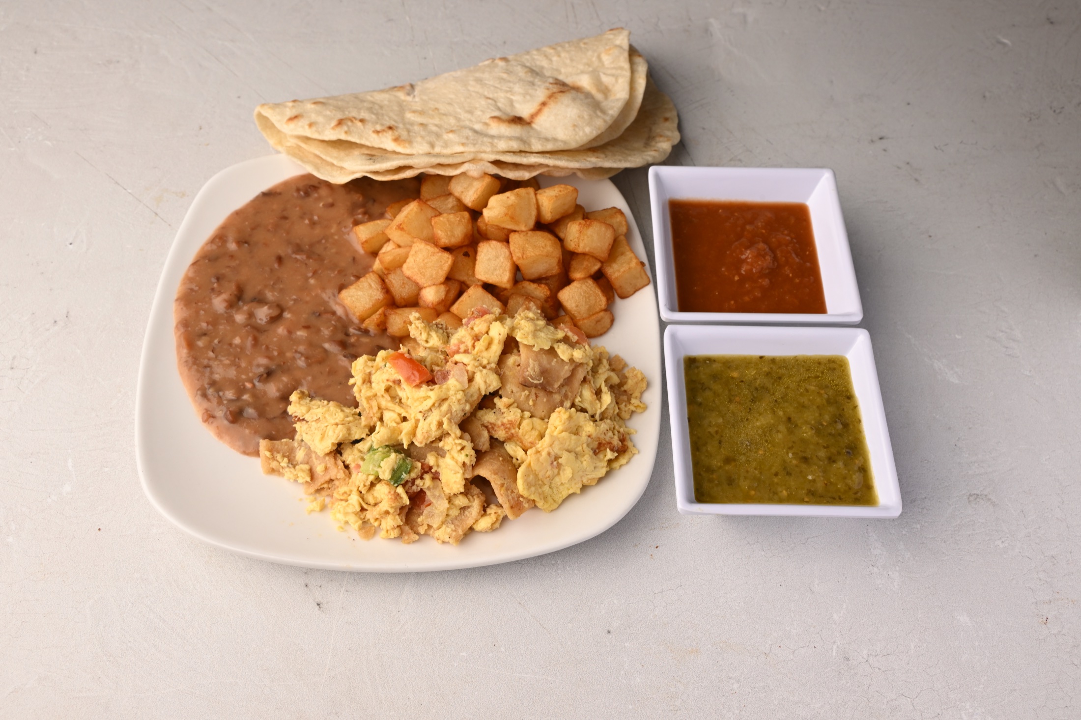Breakfast plate with eggs, beans, potatoes, tortillas, and salsa