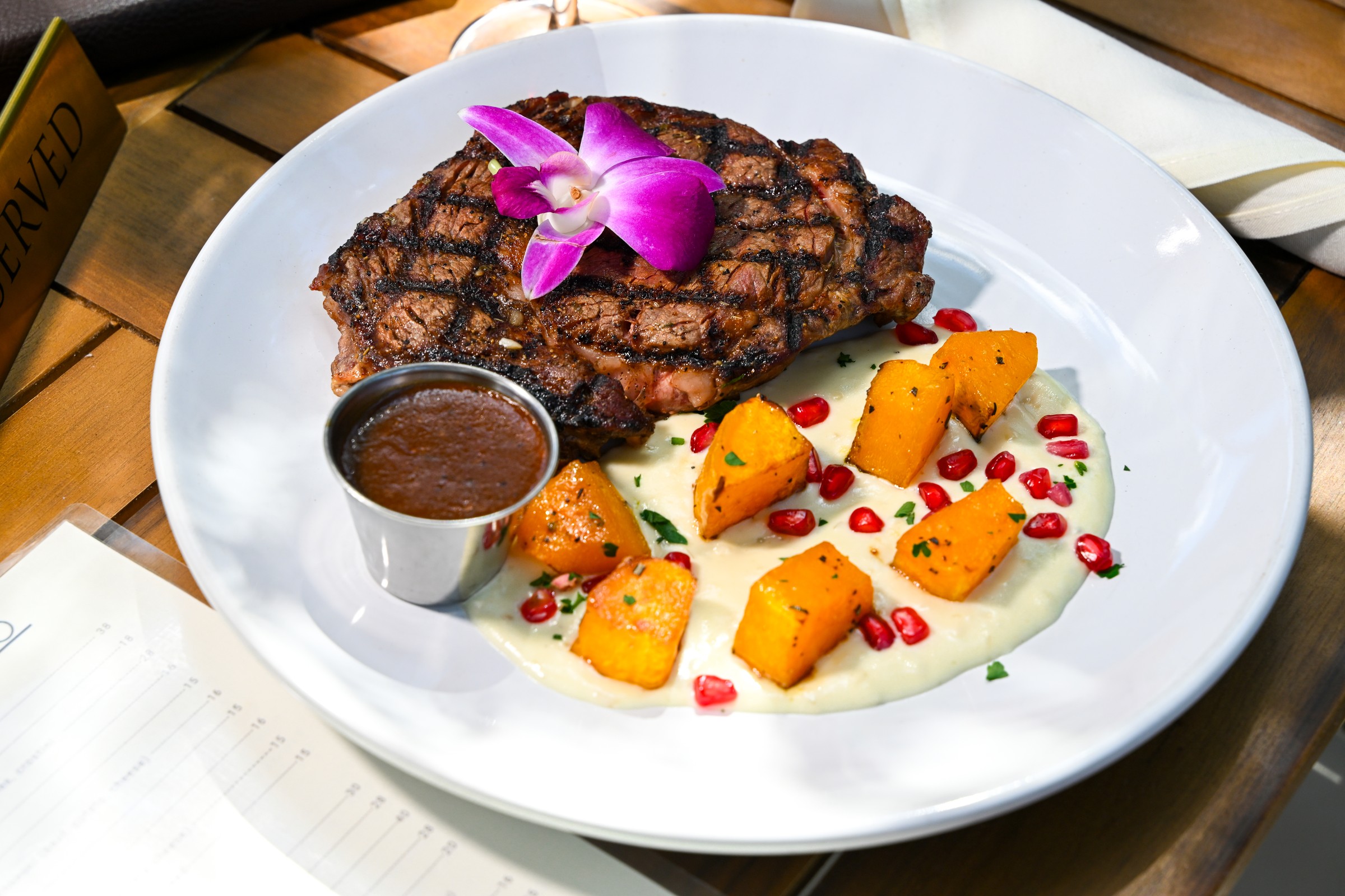 Grilled steak with squash, sauce, and pomegranate seeds