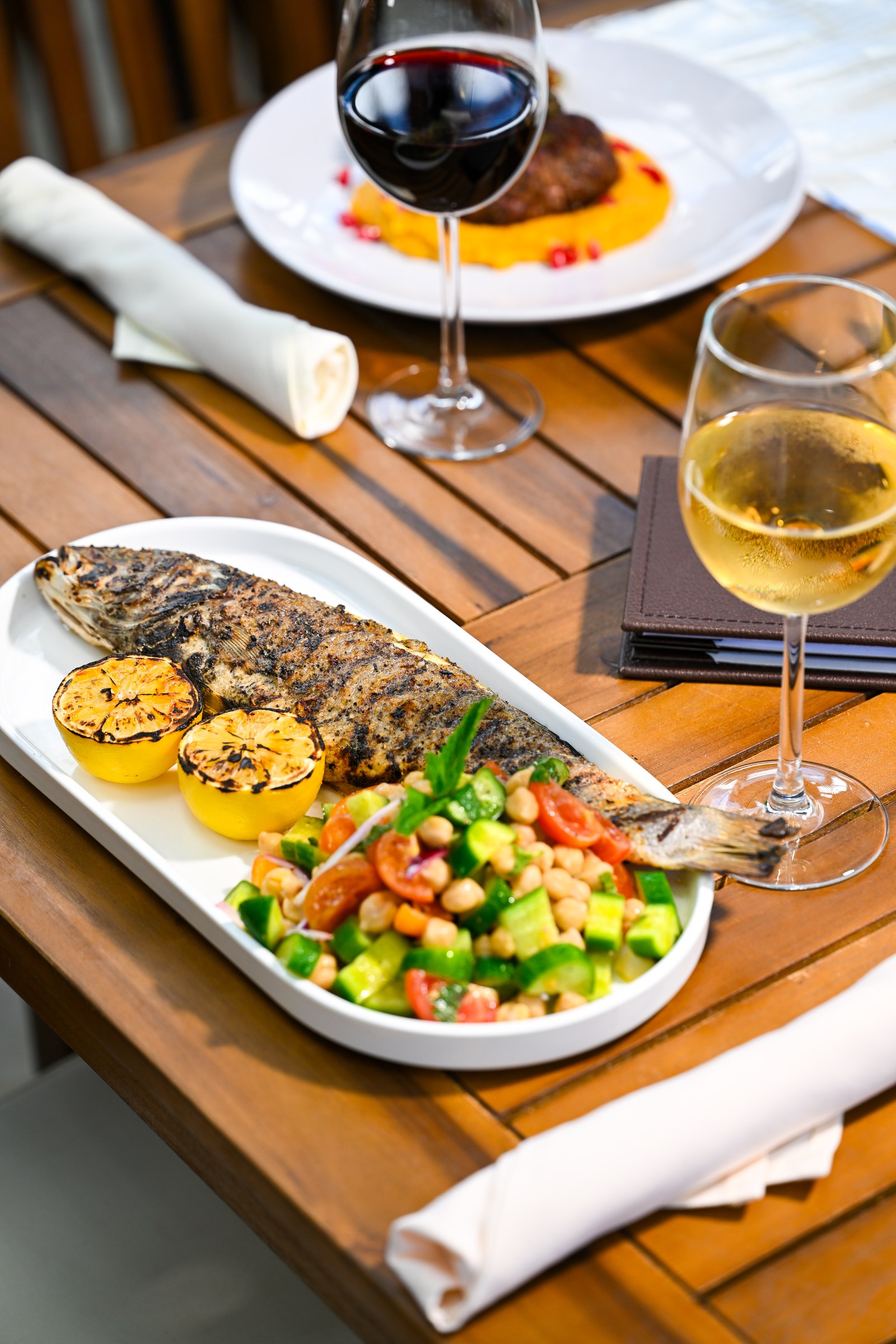 Whole grilled fish with charred lemons and a fresh vegetable salad