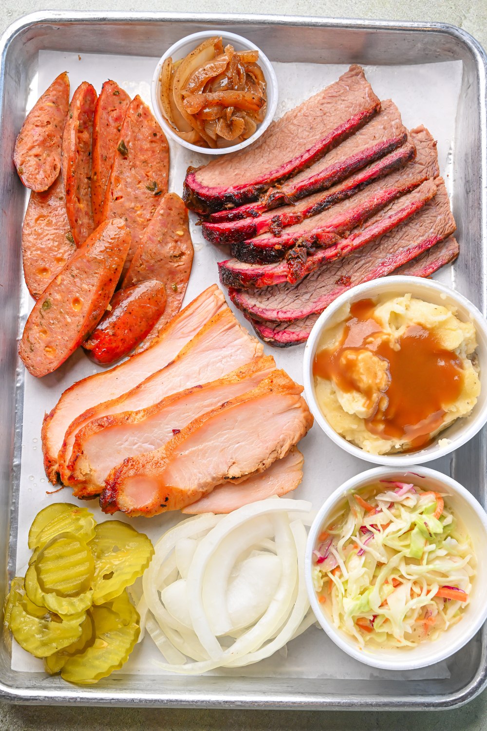 Sliced brisket, sausage, pickles, slaw, and sides on a plate