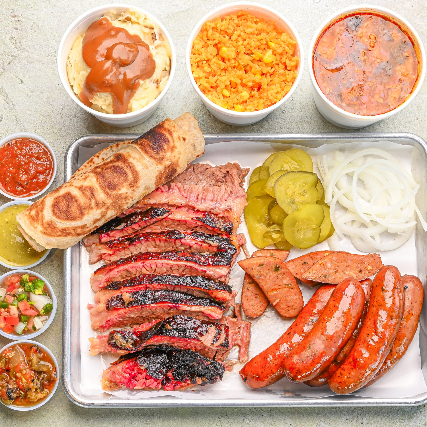 Overhead Texas Pack tray with sliced brisket, sausages, bread, and side bowls